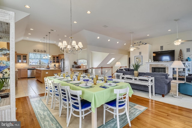 dining room featuring recessed lighting, ceiling fan with notable chandelier, a fireplace, light wood-style flooring, and high vaulted ceiling