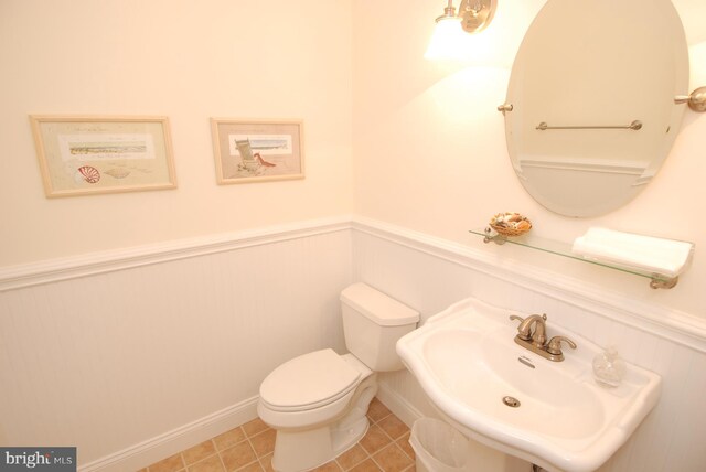 half bathroom with tile patterned flooring, toilet, wainscoting, and a sink