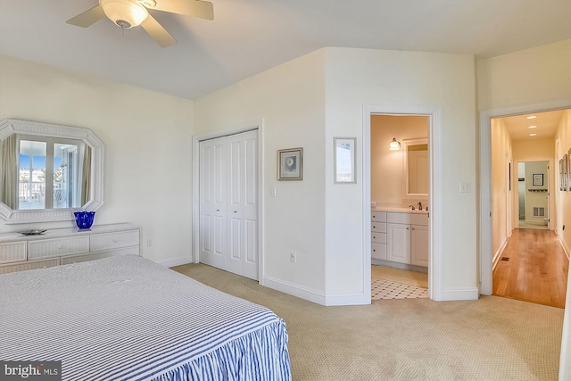 bedroom featuring ensuite bathroom, a sink, a closet, baseboards, and light colored carpet