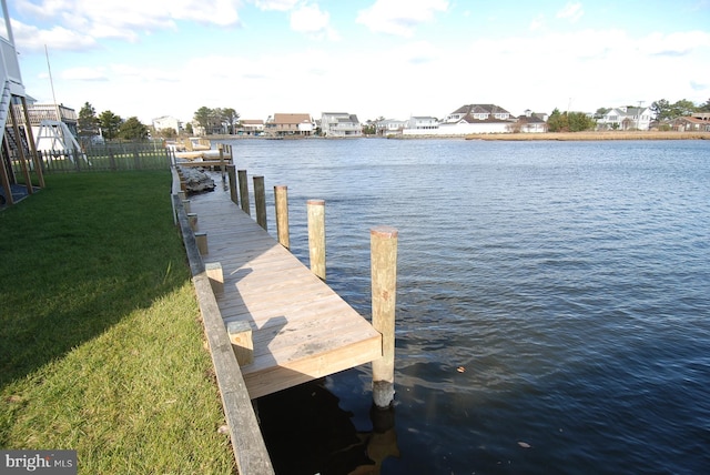 dock area featuring a water view, a lawn, and fence