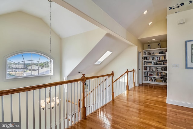 hallway with high vaulted ceiling, a skylight, recessed lighting, wood-type flooring, and an upstairs landing