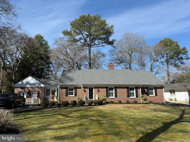 view of front facade with brick siding, a chimney, a front yard, and roof with shingles