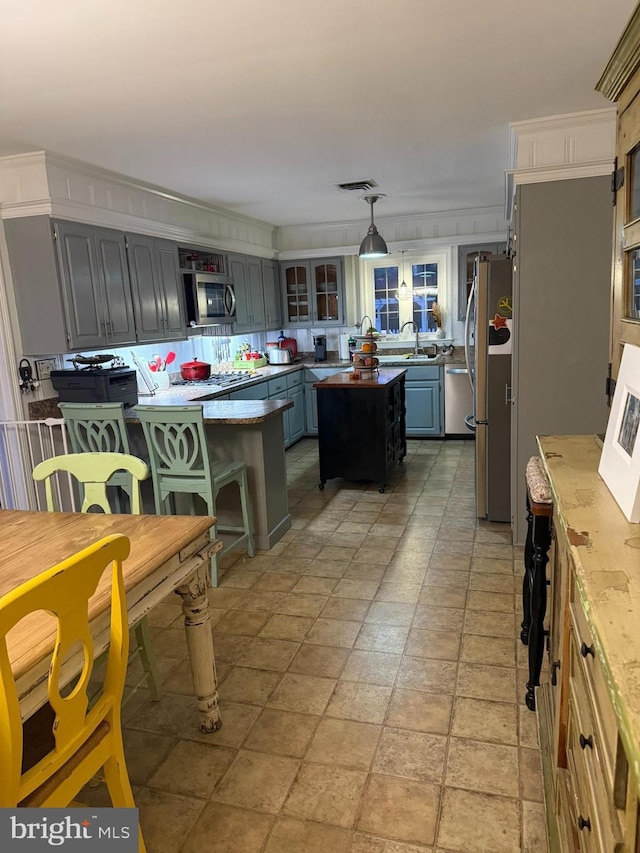 kitchen with visible vents, a center island, glass insert cabinets, stainless steel appliances, and a sink