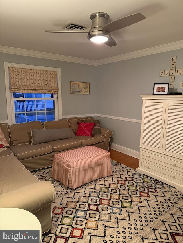 living area featuring wood finished floors, baseboards, visible vents, ornamental molding, and ceiling fan