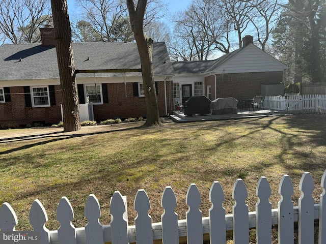 rear view of property featuring brick siding, fence, roof with shingles, a chimney, and a yard