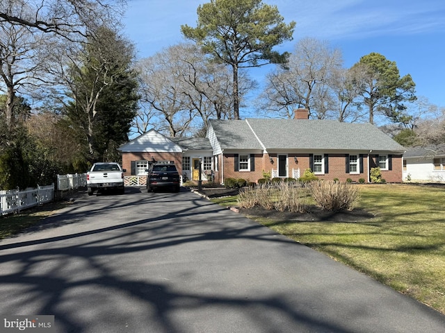 ranch-style house with fence, driveway, a chimney, a front lawn, and brick siding