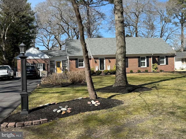 view of front of property featuring brick siding, a shingled roof, aphalt driveway, a front yard, and an attached garage