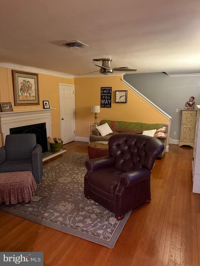 living room featuring visible vents, a fireplace with raised hearth, hardwood / wood-style floors, crown molding, and baseboards