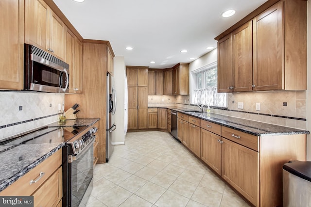 kitchen featuring light tile patterned floors, dark stone counters, a sink, appliances with stainless steel finishes, and brown cabinets