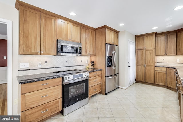 kitchen with dark stone countertops, light tile patterned floors, brown cabinets, appliances with stainless steel finishes, and tasteful backsplash