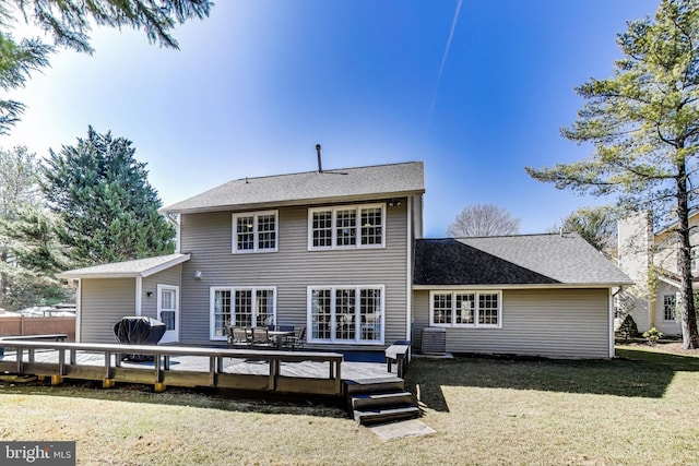 rear view of house with a deck, a yard, and roof with shingles