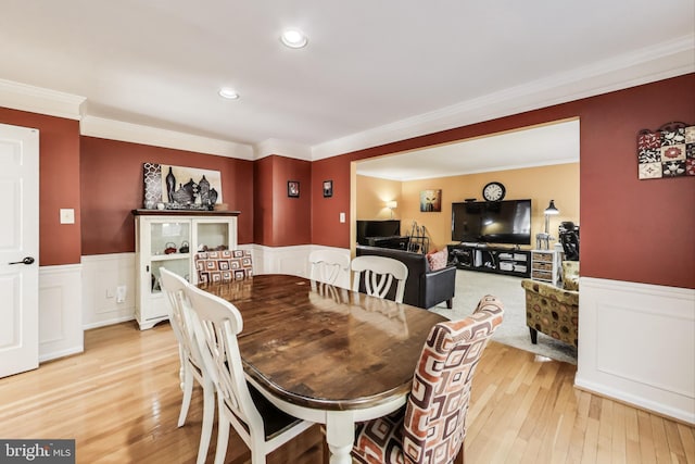 dining space featuring light wood-style flooring, wainscoting, and ornamental molding