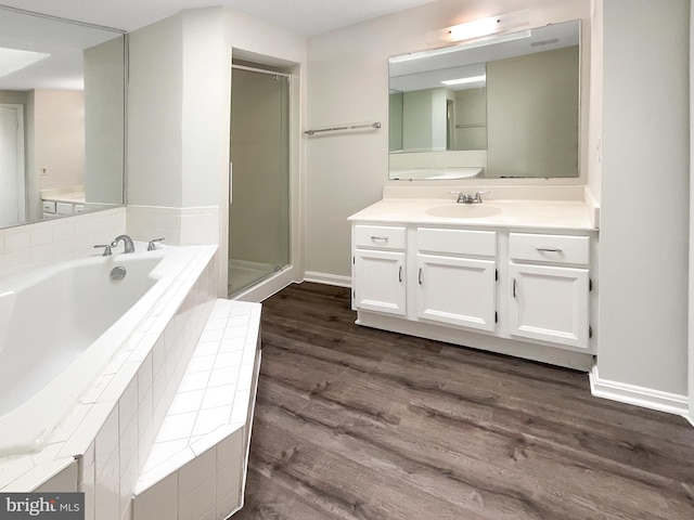 bathroom featuring a stall shower, wood finished floors, baseboards, a bath, and vanity