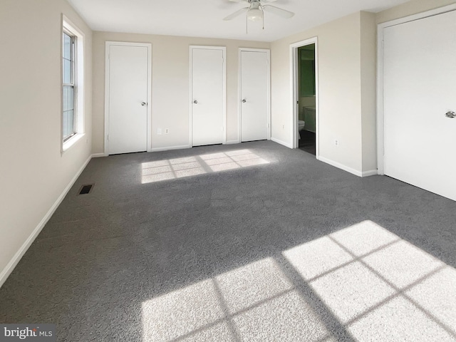 unfurnished bedroom featuring carpet, baseboards, visible vents, ensuite bath, and two closets