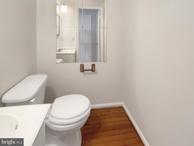 half bath featuring baseboards, toilet, wood finished floors, and vanity