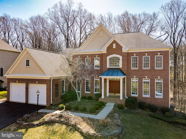 colonial inspired home featuring brick siding, driveway, a garage, and roof with shingles