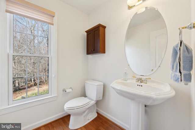 bathroom featuring baseboards, toilet, a healthy amount of sunlight, and wood finished floors