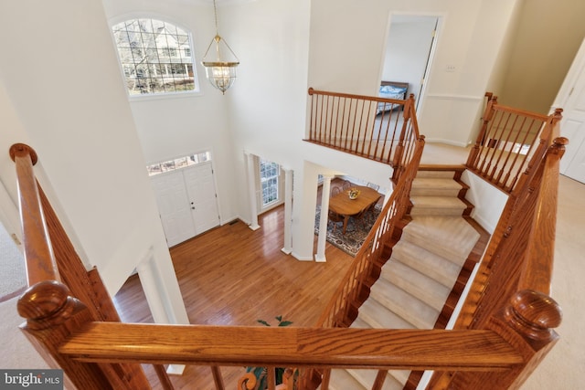 stairs featuring wood finished floors, baseboards, a towering ceiling, and a chandelier