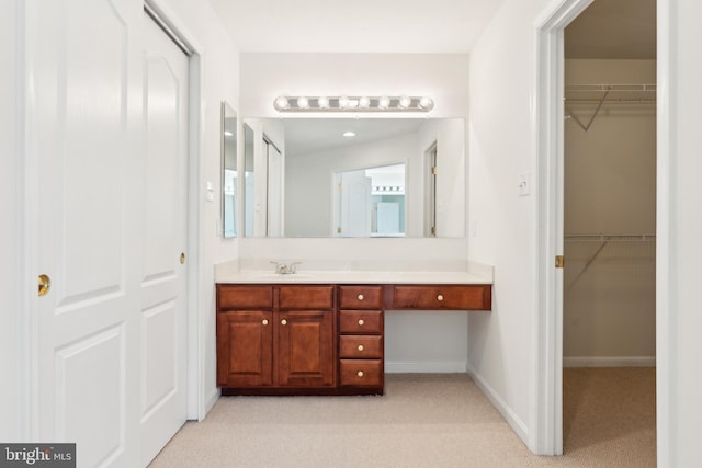 bathroom featuring a walk in closet, vanity, carpet, and baseboards