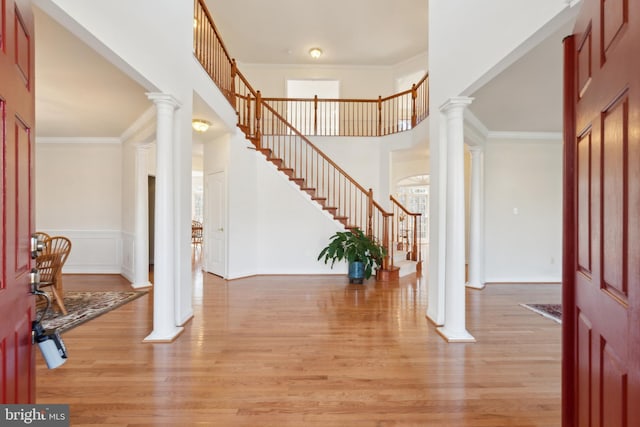 foyer entrance featuring light wood-type flooring, decorative columns, ornamental molding, and stairway