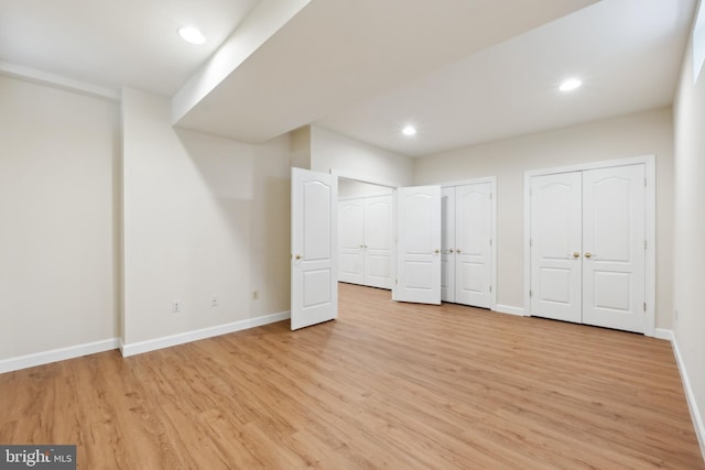 unfurnished bedroom featuring recessed lighting, light wood-type flooring, baseboards, and multiple closets