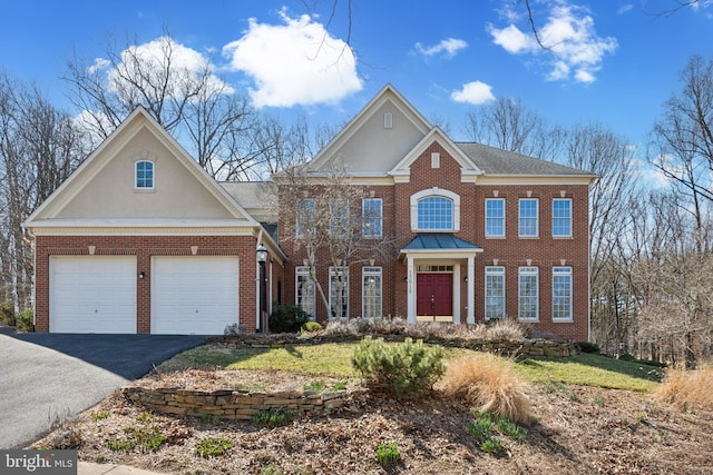 colonial inspired home featuring aphalt driveway, brick siding, a garage, and stucco siding