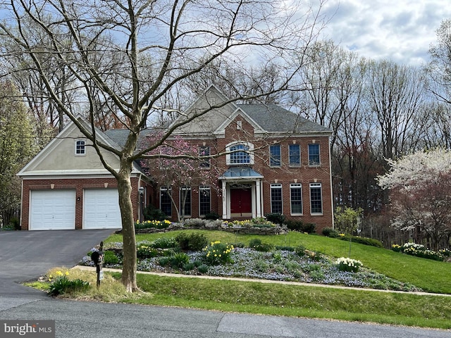 colonial house with brick siding, driveway, an attached garage, and a front yard