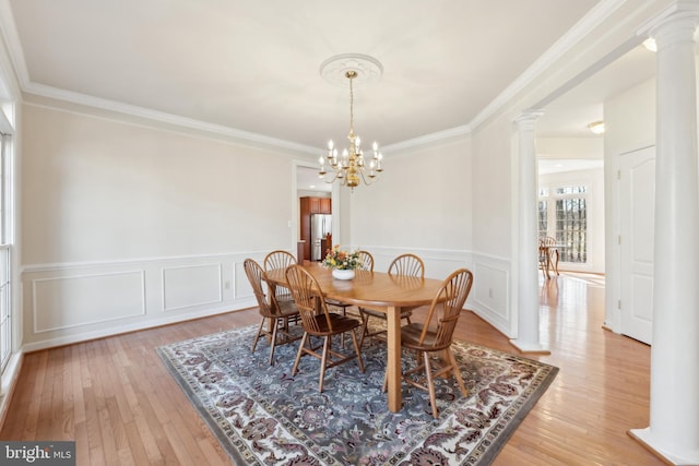 dining space featuring light wood finished floors, ornamental molding, decorative columns, wainscoting, and a notable chandelier