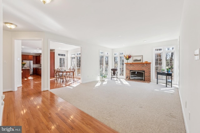 unfurnished living room with baseboards, light colored carpet, a fireplace, and light wood finished floors