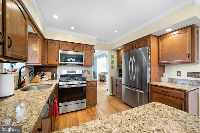 kitchen with a sink, ornamental molding, light stone countertops, and stainless steel appliances