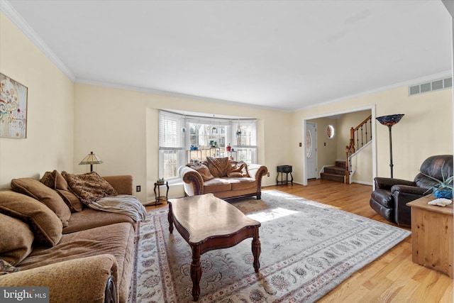 living area with visible vents, light wood-style flooring, crown molding, baseboards, and stairs