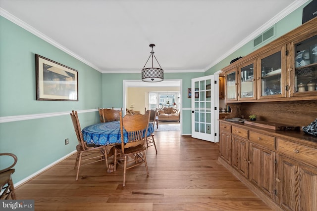 dining area featuring baseboards, light wood-style floors, visible vents, and ornamental molding