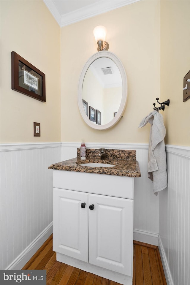 bathroom with a wainscoted wall, visible vents, wood finished floors, crown molding, and vanity