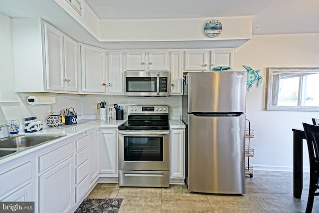 kitchen featuring baseboards, light countertops, appliances with stainless steel finishes, white cabinetry, and a sink