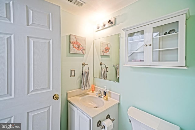 half bath featuring visible vents, toilet, and vanity