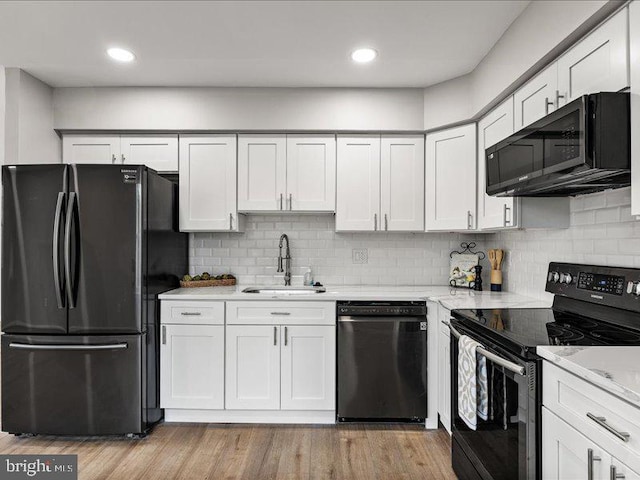 kitchen with light wood-style flooring, a sink, decorative backsplash, black appliances, and white cabinets