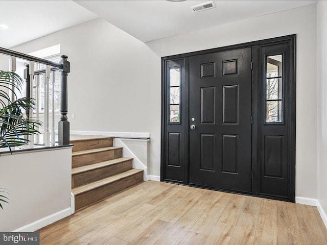 foyer featuring a wealth of natural light, visible vents, stairs, and wood finished floors