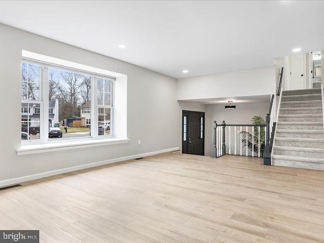 unfurnished living room with visible vents, baseboards, wood finished floors, and stairs