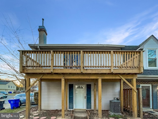 back of house with roof with shingles, central AC unit, a deck, and a chimney