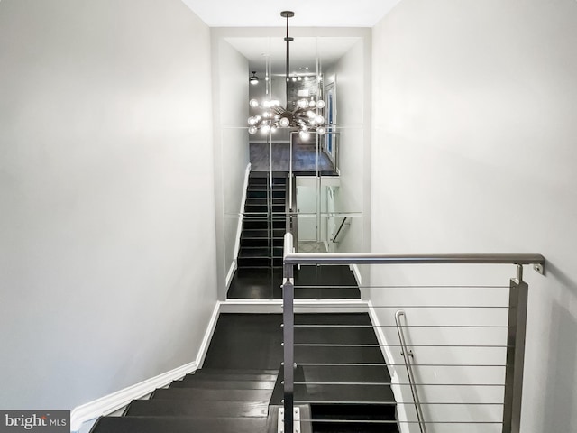 stairway featuring baseboards, an inviting chandelier, and wood finished floors