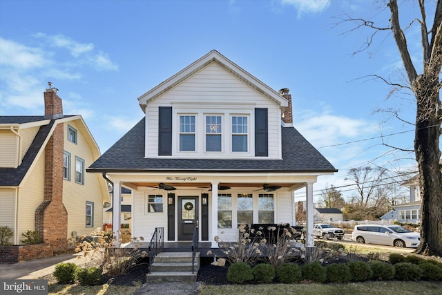 view of front of house featuring ceiling fan, a porch, a chimney, and a shingled roof