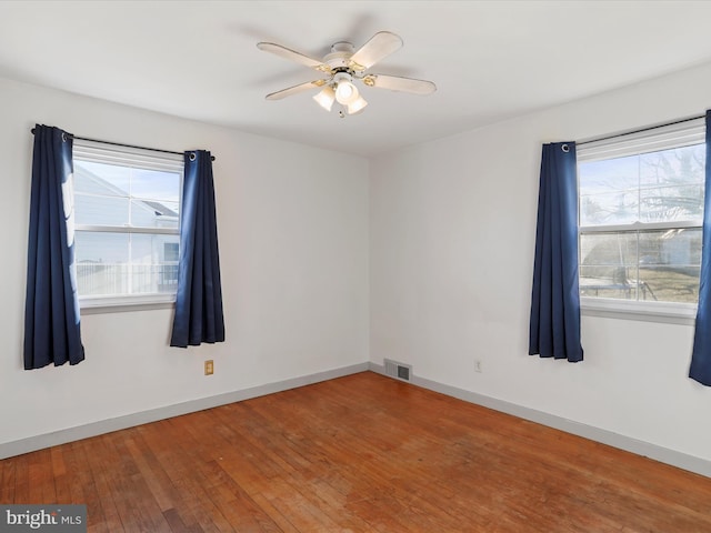 spare room featuring a healthy amount of sunlight, visible vents, wood-type flooring, and baseboards