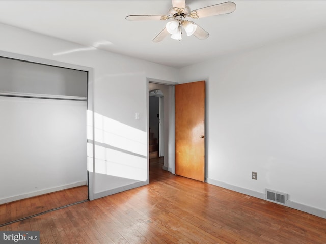 unfurnished bedroom featuring visible vents, baseboards, hardwood / wood-style floors, a closet, and a ceiling fan