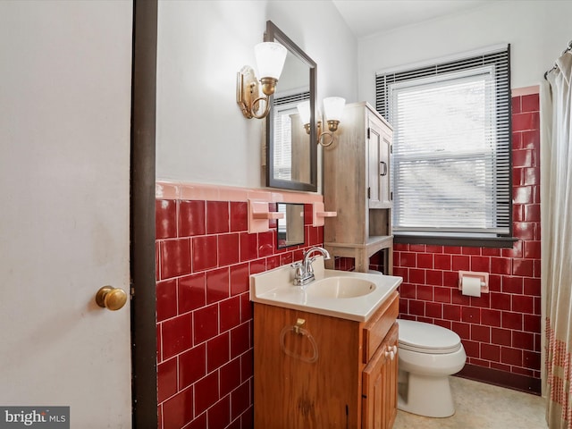 bathroom with toilet, tile walls, wainscoting, and vanity