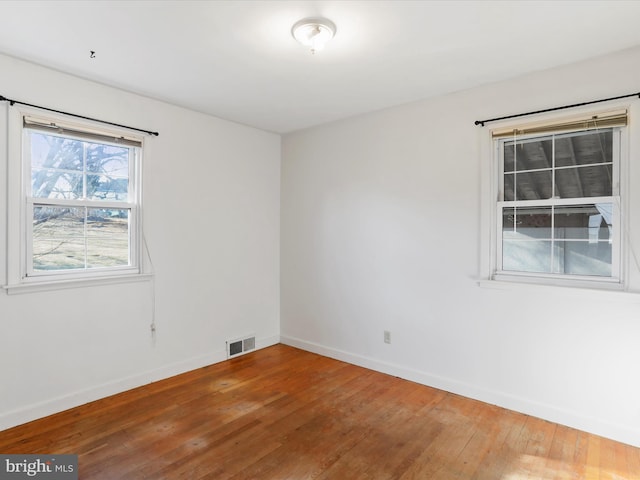 unfurnished room featuring hardwood / wood-style floors, baseboards, and visible vents