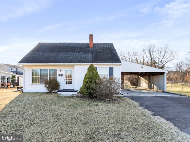 view of front of property with a front yard, a shingled roof, a chimney, a carport, and aphalt driveway