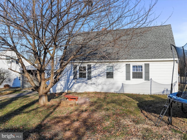 back of house featuring a chimney, a trampoline, roof with shingles, and a lawn