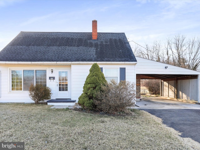 view of front of property featuring an attached carport, a shingled roof, a front yard, a chimney, and driveway