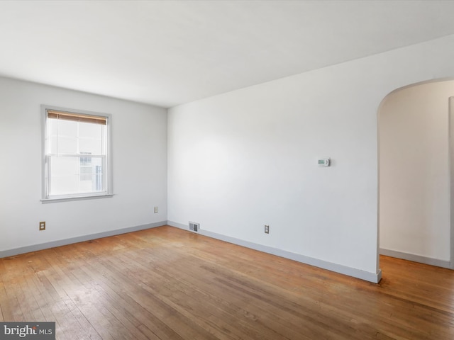 unfurnished room with arched walkways, visible vents, baseboards, and hardwood / wood-style flooring