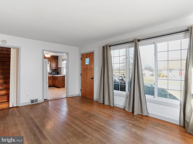 unfurnished living room with hardwood / wood-style floors, baseboards, visible vents, and a wealth of natural light